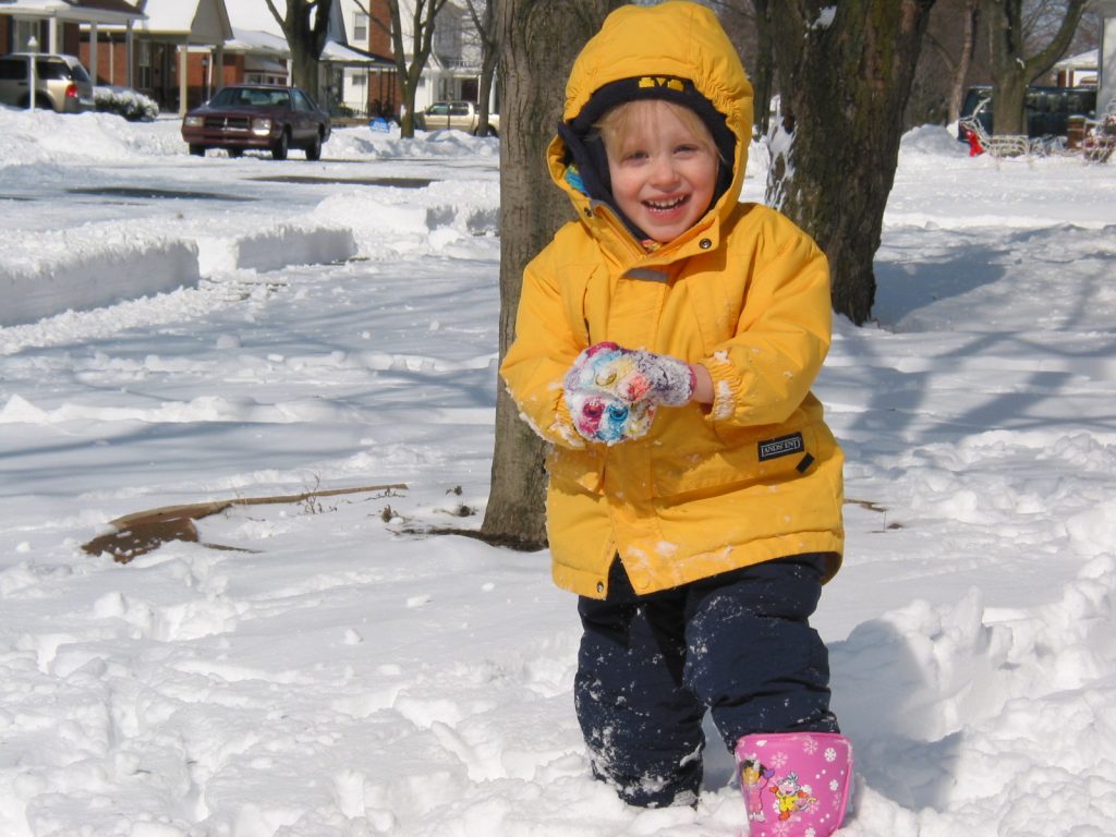 A child playing in the snow with a snowball.