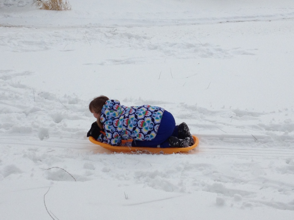 Ways to embrace winter: A child sledding down a hill. 