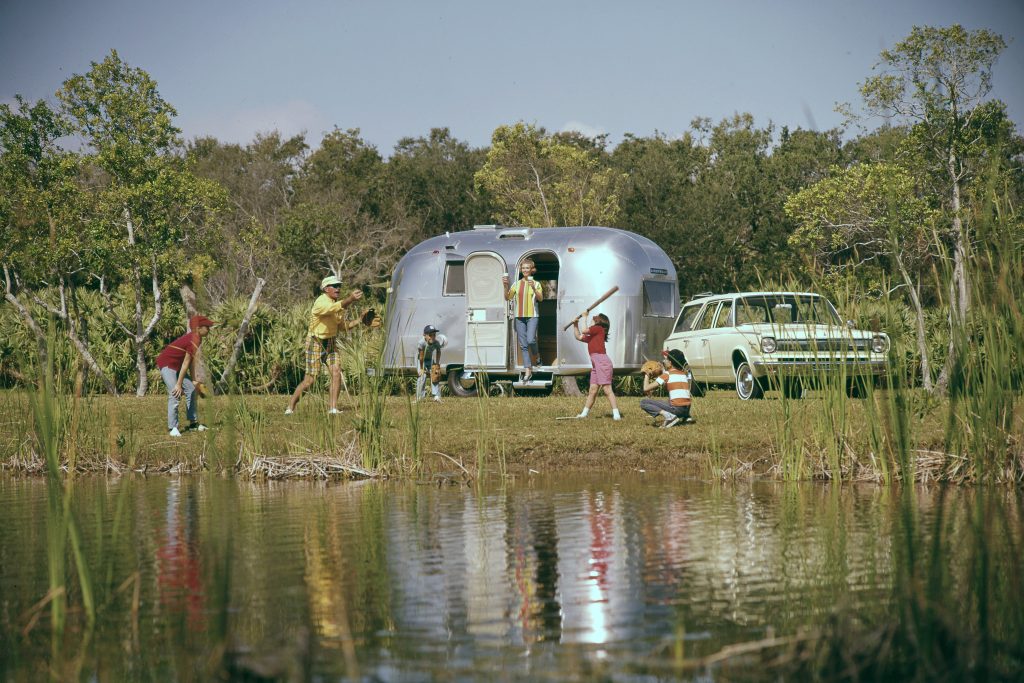 Vintage photo of an Airstream trailer with a family playing baseball out front. Multigenerational vacation tips - Relive childhood memories.
